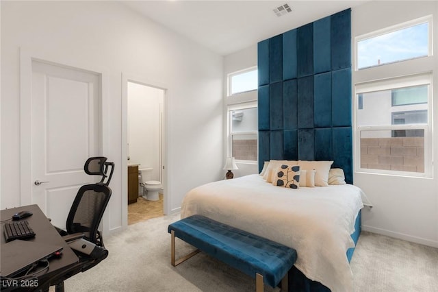 bedroom featuring baseboards, visible vents, ensuite bathroom, and light carpet