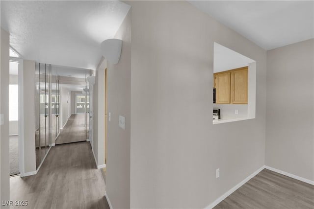 corridor with wood finished floors, baseboards, and a wealth of natural light