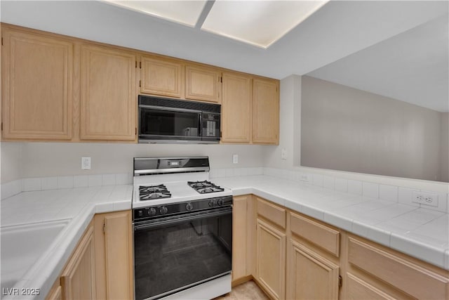 kitchen featuring a sink, gas range oven, black microwave, and light brown cabinetry