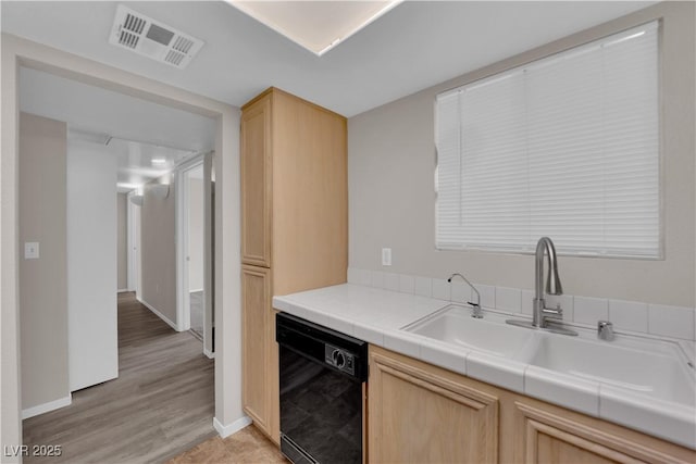 kitchen featuring visible vents, light brown cabinets, light wood-type flooring, black dishwasher, and a sink