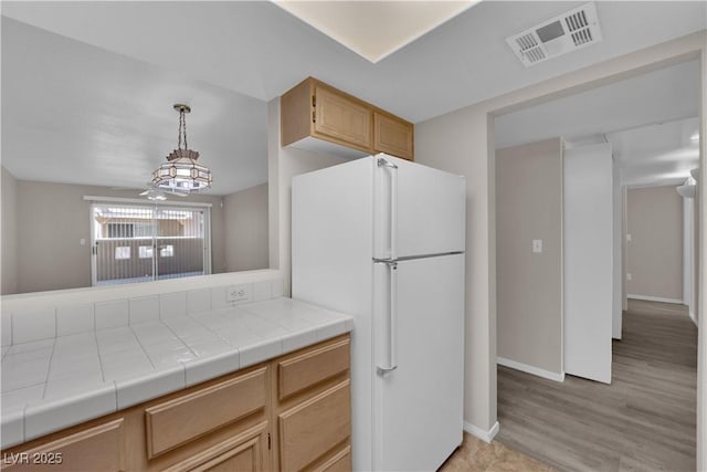 kitchen with visible vents, baseboards, tile counters, decorative light fixtures, and freestanding refrigerator