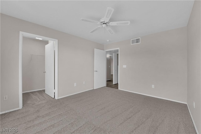 unfurnished bedroom featuring carpet, baseboards, visible vents, ceiling fan, and a spacious closet