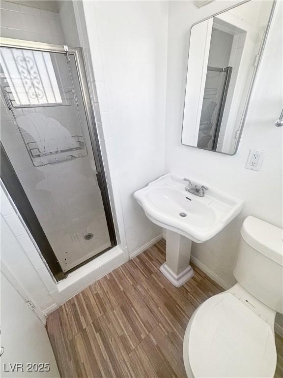 bathroom featuring toilet, wood finished floors, a stall shower, and baseboards