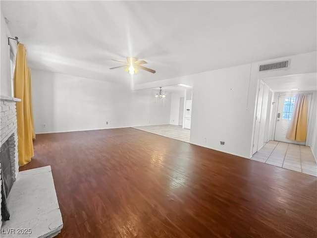 unfurnished living room featuring ceiling fan with notable chandelier, a fireplace, visible vents, and light wood-type flooring