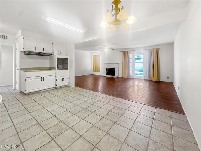 unfurnished living room featuring ceiling fan with notable chandelier, light tile patterned flooring, and a fireplace