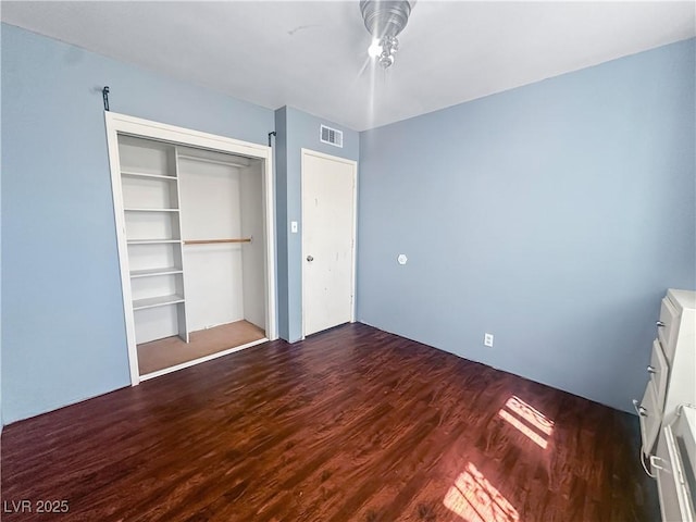 unfurnished bedroom with a closet, visible vents, ceiling fan, and wood finished floors