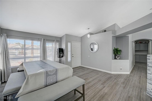 bedroom with wood finished floors, baseboards, visible vents, arched walkways, and vaulted ceiling