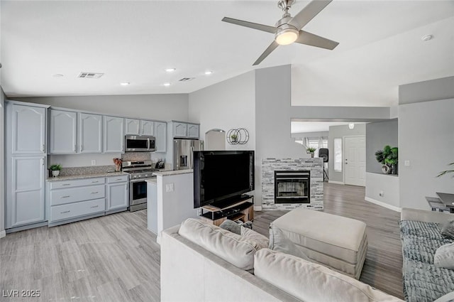 living area featuring ceiling fan, visible vents, light wood-style flooring, and vaulted ceiling