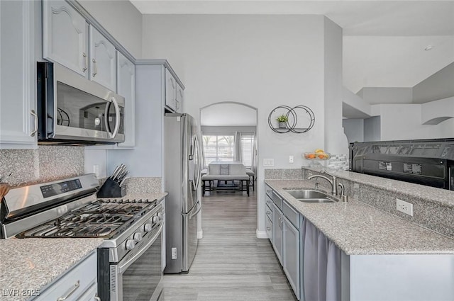 kitchen featuring a sink, light stone counters, arched walkways, appliances with stainless steel finishes, and light wood finished floors