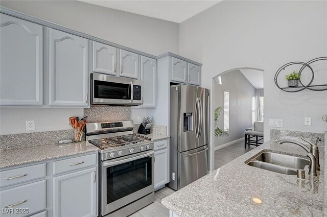 kitchen with light stone counters, light wood-style flooring, arched walkways, a sink, and stainless steel appliances