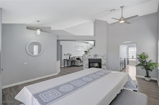 bedroom with wood finished floors, visible vents, baseboards, vaulted ceiling, and a tiled fireplace