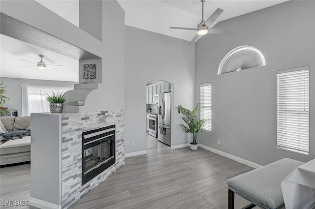 living room with baseboards, wood finished floors, a glass covered fireplace, and a ceiling fan