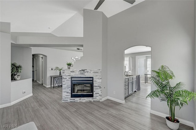 unfurnished living room featuring visible vents, light wood finished floors, baseboards, arched walkways, and a glass covered fireplace