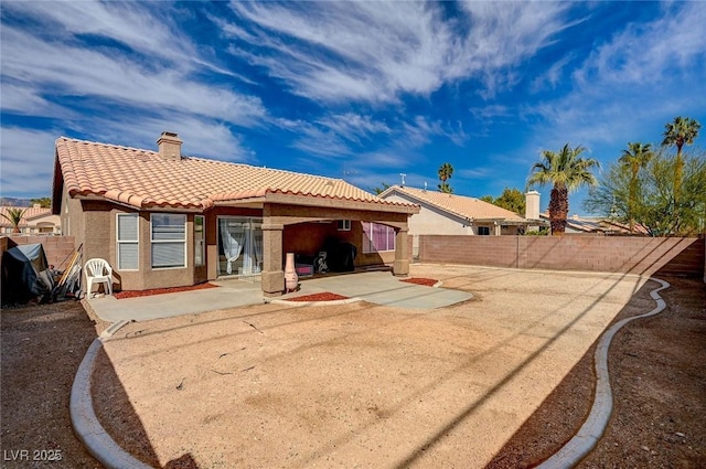 rear view of house with a tile roof, stucco siding, a chimney, a fenced backyard, and a patio