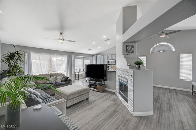 living room featuring baseboards, ceiling fan, light wood-type flooring, vaulted ceiling, and a stone fireplace