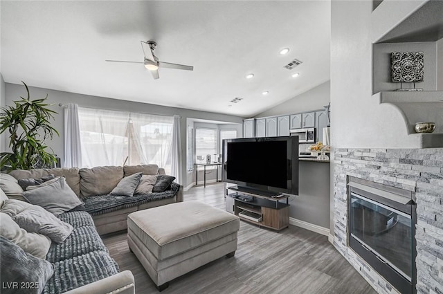 living area with visible vents, wood finished floors, a stone fireplace, lofted ceiling, and ceiling fan