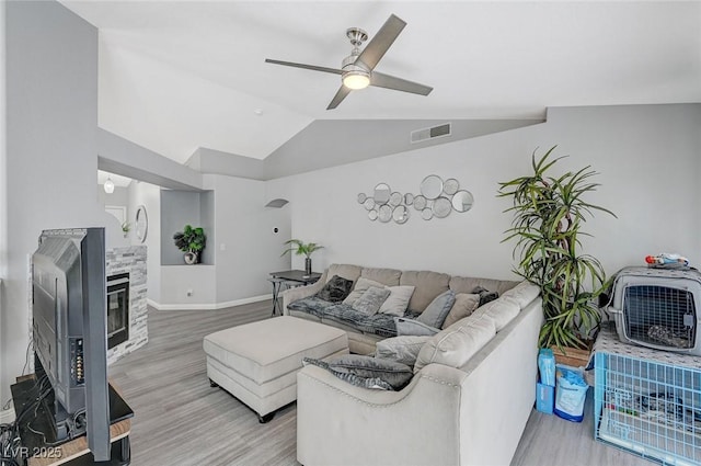 living room featuring visible vents, light wood finished floors, ceiling fan, vaulted ceiling, and a glass covered fireplace