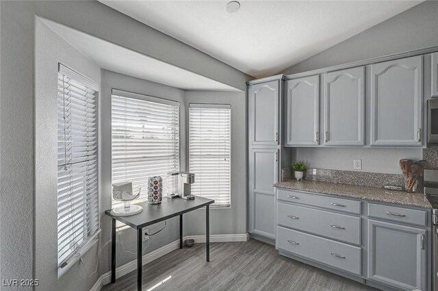 kitchen with baseboards, lofted ceiling, gray cabinetry, stainless steel microwave, and light wood-type flooring