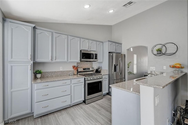 kitchen with a peninsula, lofted ceiling, arched walkways, a sink, and stainless steel appliances