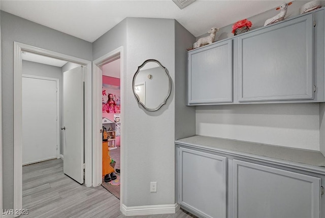 hall with baseboards, visible vents, and light wood finished floors