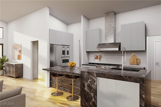 kitchen featuring wall chimney range hood, a kitchen bar, gray cabinets, appliances with stainless steel finishes, and a sink