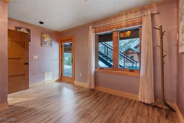 empty room featuring visible vents, ornamental molding, wood finished floors, baseboards, and a textured wall