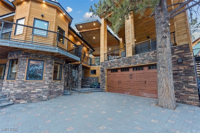 view of front of home featuring a balcony, a garage, and stone siding