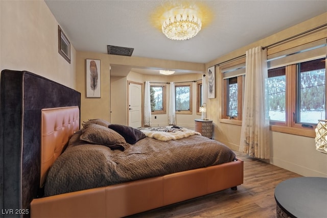 bedroom featuring visible vents, baseboards, an inviting chandelier, and wood finished floors