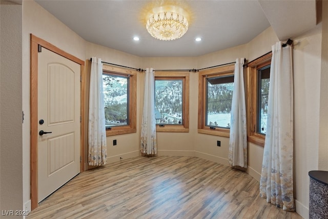 doorway to outside featuring plenty of natural light, light wood-type flooring, and an inviting chandelier