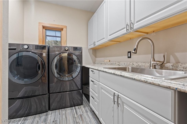 laundry area featuring a sink, cabinet space, light wood finished floors, and washer and clothes dryer