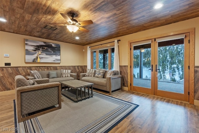 living area with a wainscoted wall, wood walls, wooden ceiling, french doors, and wood finished floors