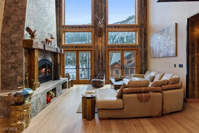 living room with a high ceiling, a stone fireplace, and wood finished floors