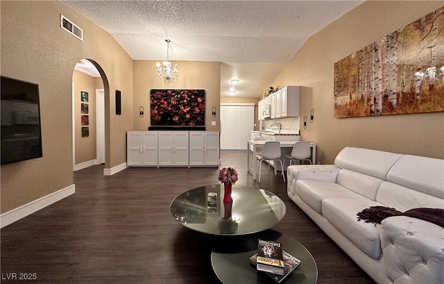 living room featuring visible vents, dark wood finished floors, vaulted ceiling, arched walkways, and a notable chandelier