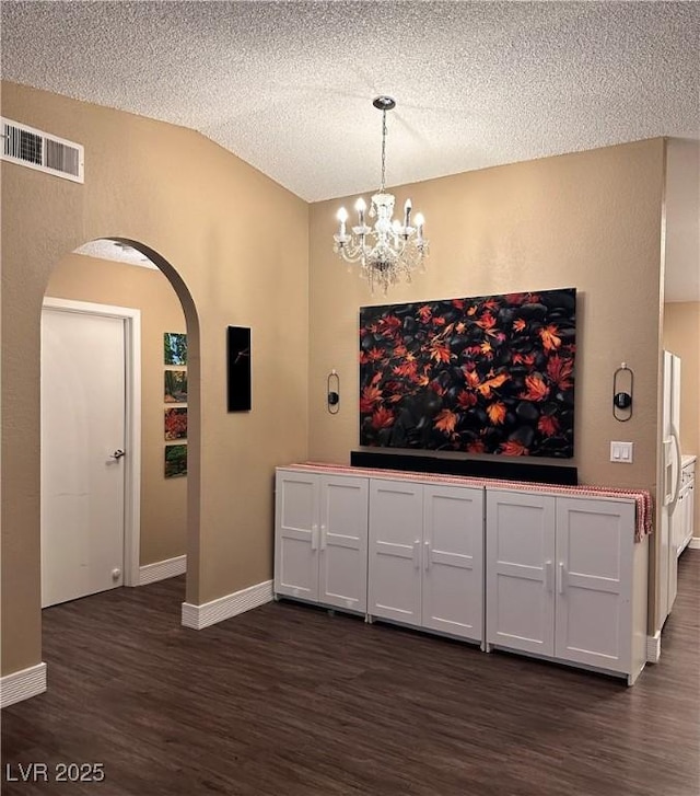 interior space featuring visible vents, a textured ceiling, dark wood finished floors, arched walkways, and baseboards