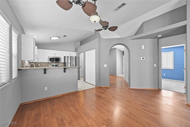 kitchen featuring arched walkways, stainless steel appliances, a ceiling fan, and vaulted ceiling