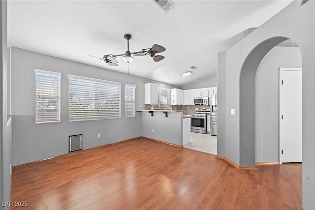 kitchen featuring visible vents, a kitchen breakfast bar, arched walkways, appliances with stainless steel finishes, and a peninsula