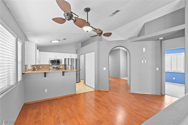 kitchen featuring visible vents, a peninsula, arched walkways, white cabinets, and appliances with stainless steel finishes