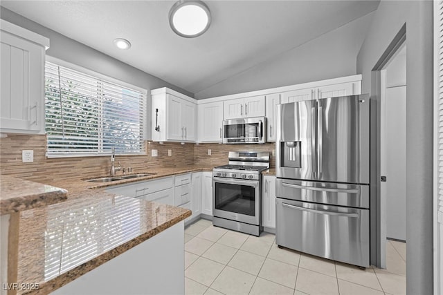 kitchen with light tile patterned floors, a sink, stainless steel appliances, vaulted ceiling, and white cabinets