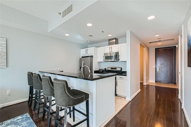 kitchen featuring visible vents, a kitchen breakfast bar, dark countertops, wood finished floors, and appliances with stainless steel finishes