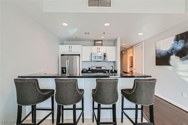 kitchen with visible vents, a breakfast bar, a sink, stainless steel appliances, and white cabinets