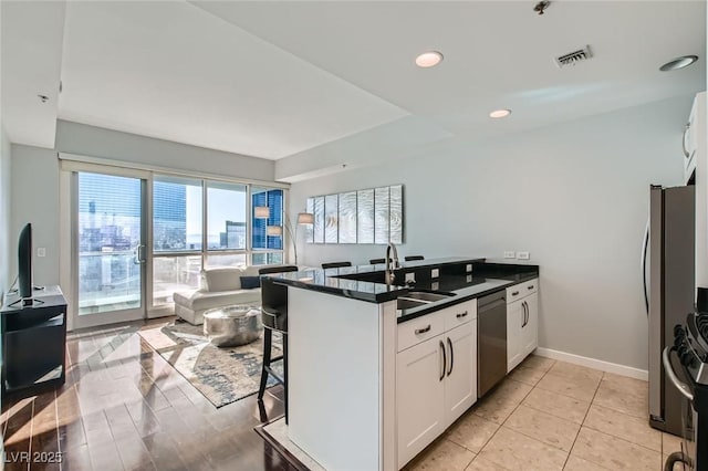 kitchen featuring visible vents, a sink, dark countertops, stainless steel appliances, and a peninsula