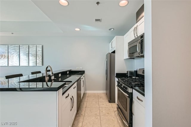 kitchen with visible vents, a peninsula, a sink, appliances with stainless steel finishes, and dark countertops