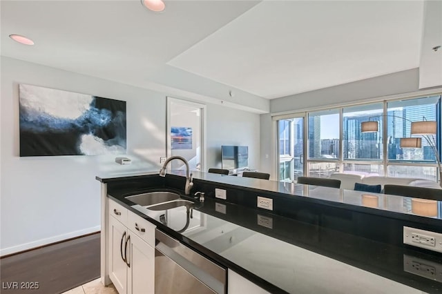 kitchen featuring a sink, stainless steel dishwasher, dark countertops, white cabinets, and baseboards