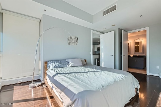 bedroom with visible vents, connected bathroom, baseboards, and wood finished floors