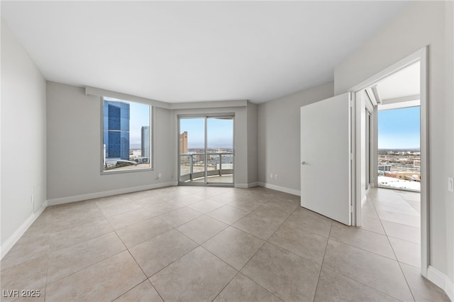 spare room featuring tile patterned floors, a view of city, a healthy amount of sunlight, and baseboards