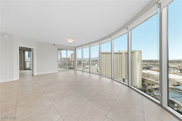 empty room featuring light tile patterned floors, floor to ceiling windows, a view of city, and baseboards