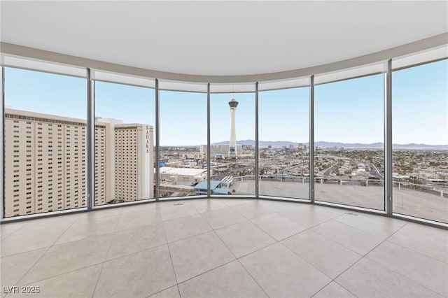 spare room featuring tile patterned flooring, floor to ceiling windows, a mountain view, and a view of city