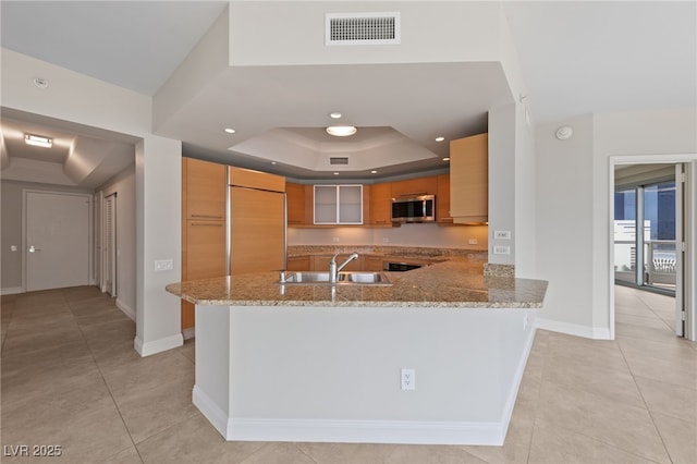 kitchen featuring light stone countertops, visible vents, a tray ceiling, built in fridge, and stainless steel microwave