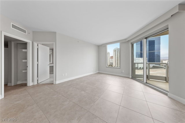 empty room featuring light tile patterned floors, visible vents, a view of city, and baseboards