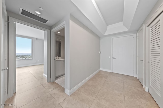 corridor featuring light tile patterned flooring, baseboards, visible vents, and a sink